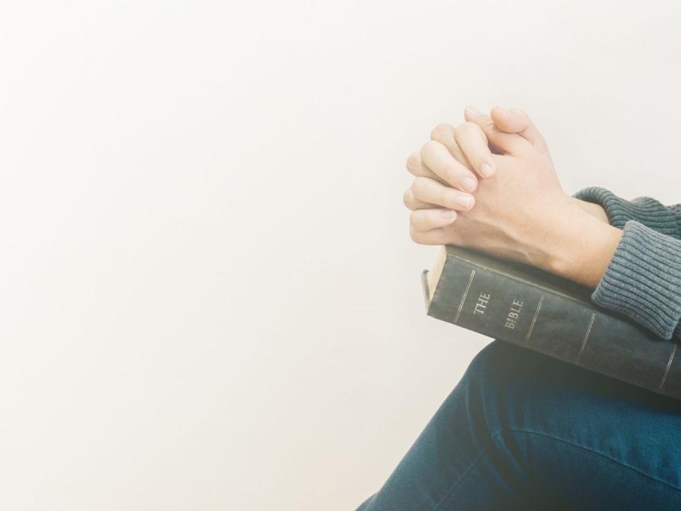 woman praying with clasped hands on open book