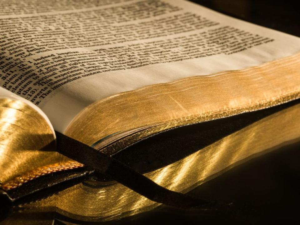 Old Bible with gold leafed pages and ribbon marking place open on burnished tabletop