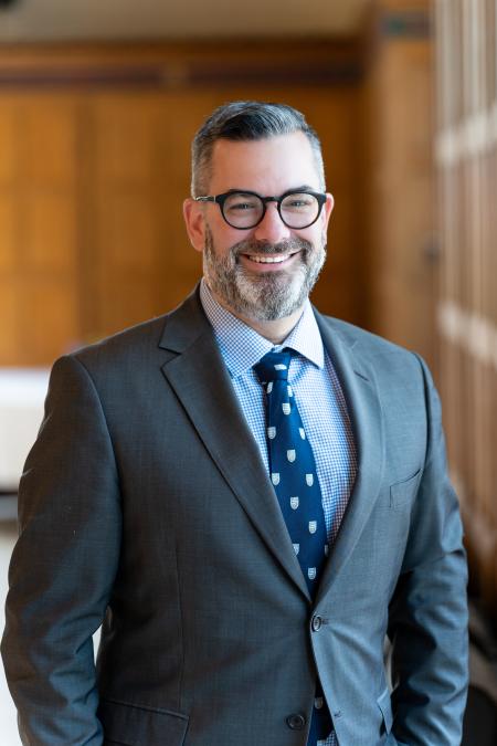 Dr Justin Stratis in Great Hall against wood panelling (2025)