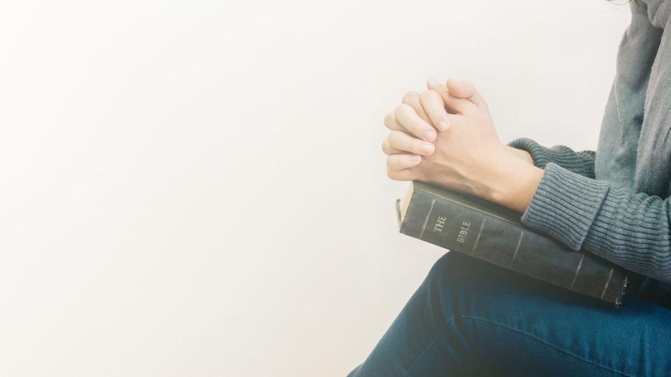 woman praying with clasped hands on open book